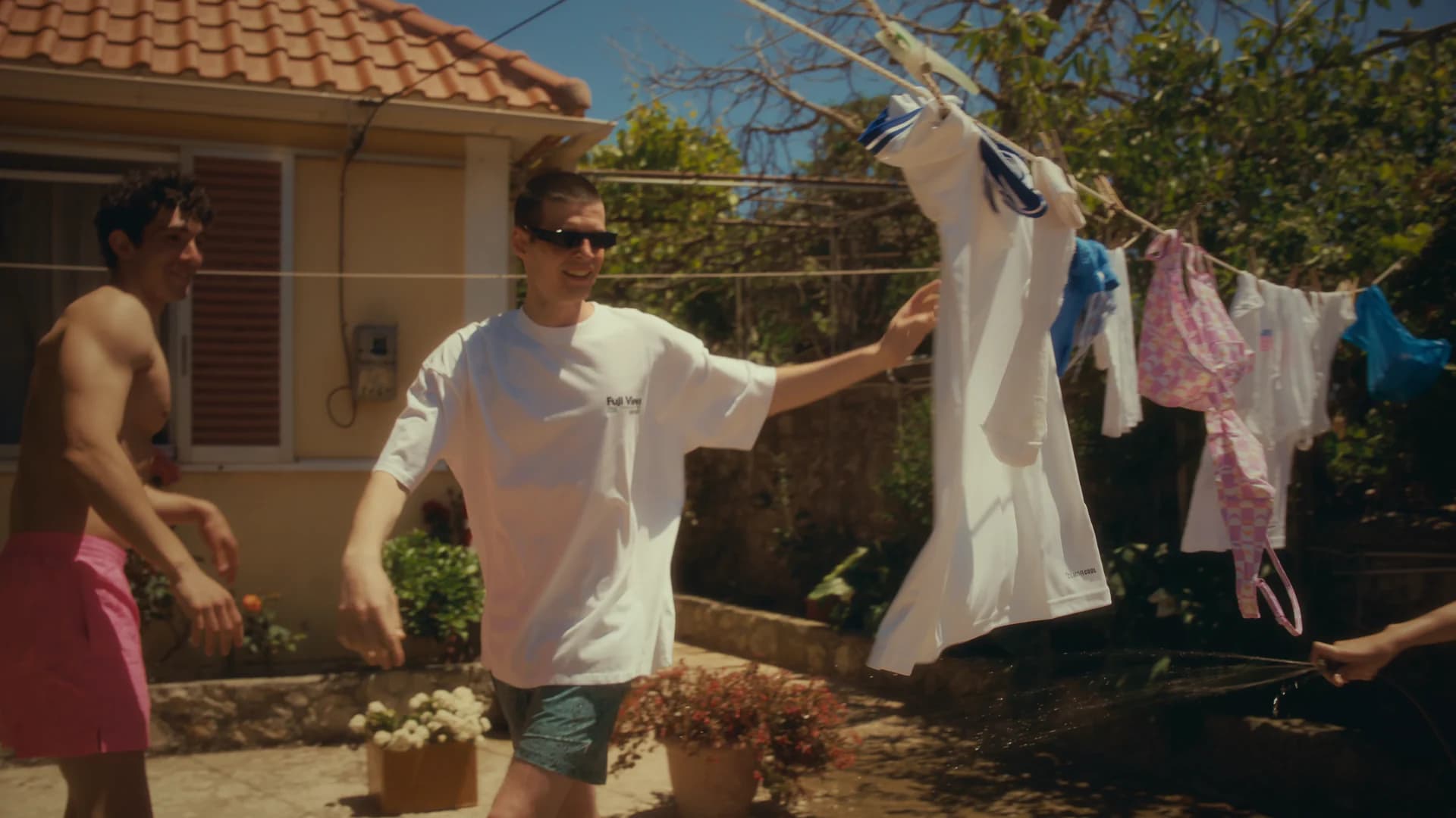 Friends laughing beside a clothesline in a bright island courtyard