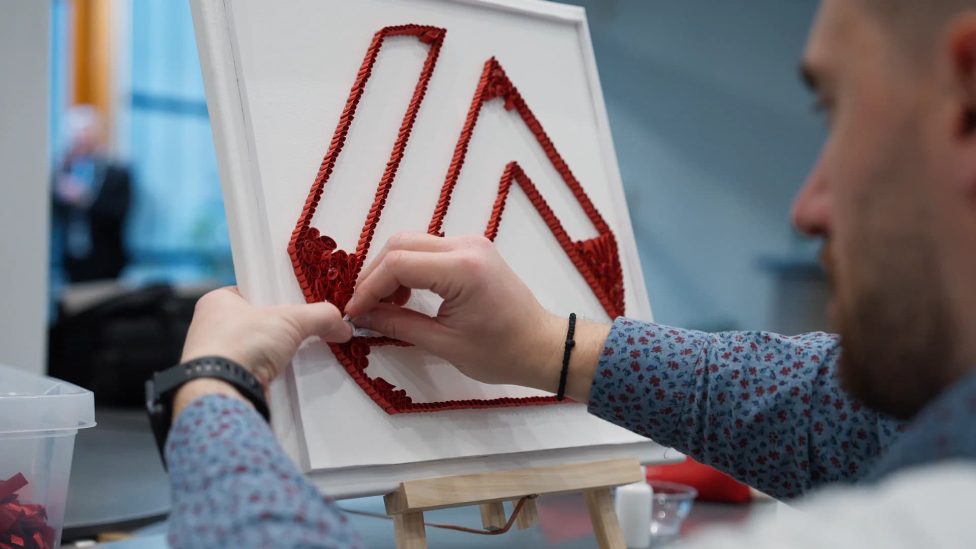 Hands shaping the red Eurobank mark in paper quilling