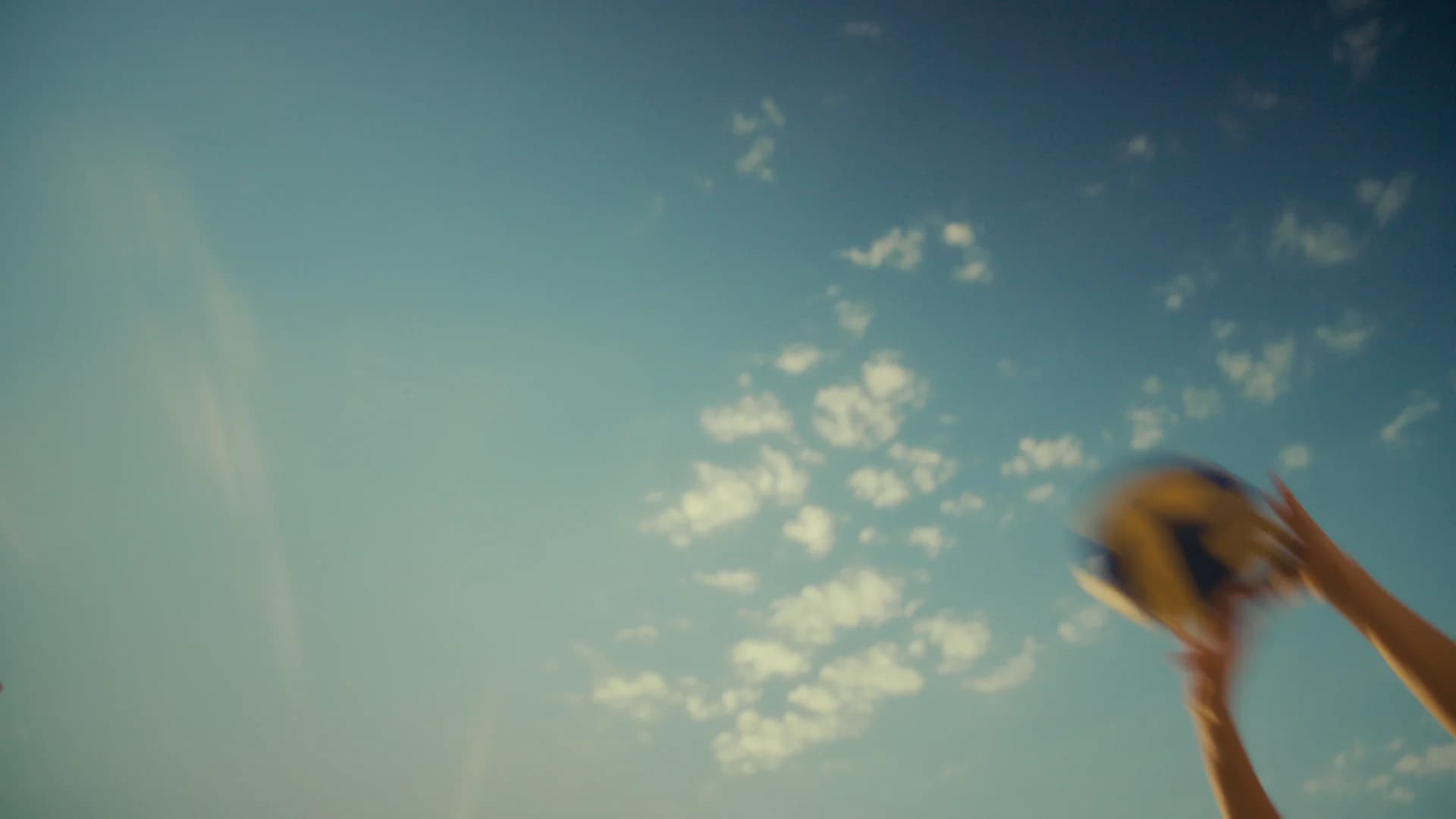 Hands throwing a ball upward into a bright blue sky
